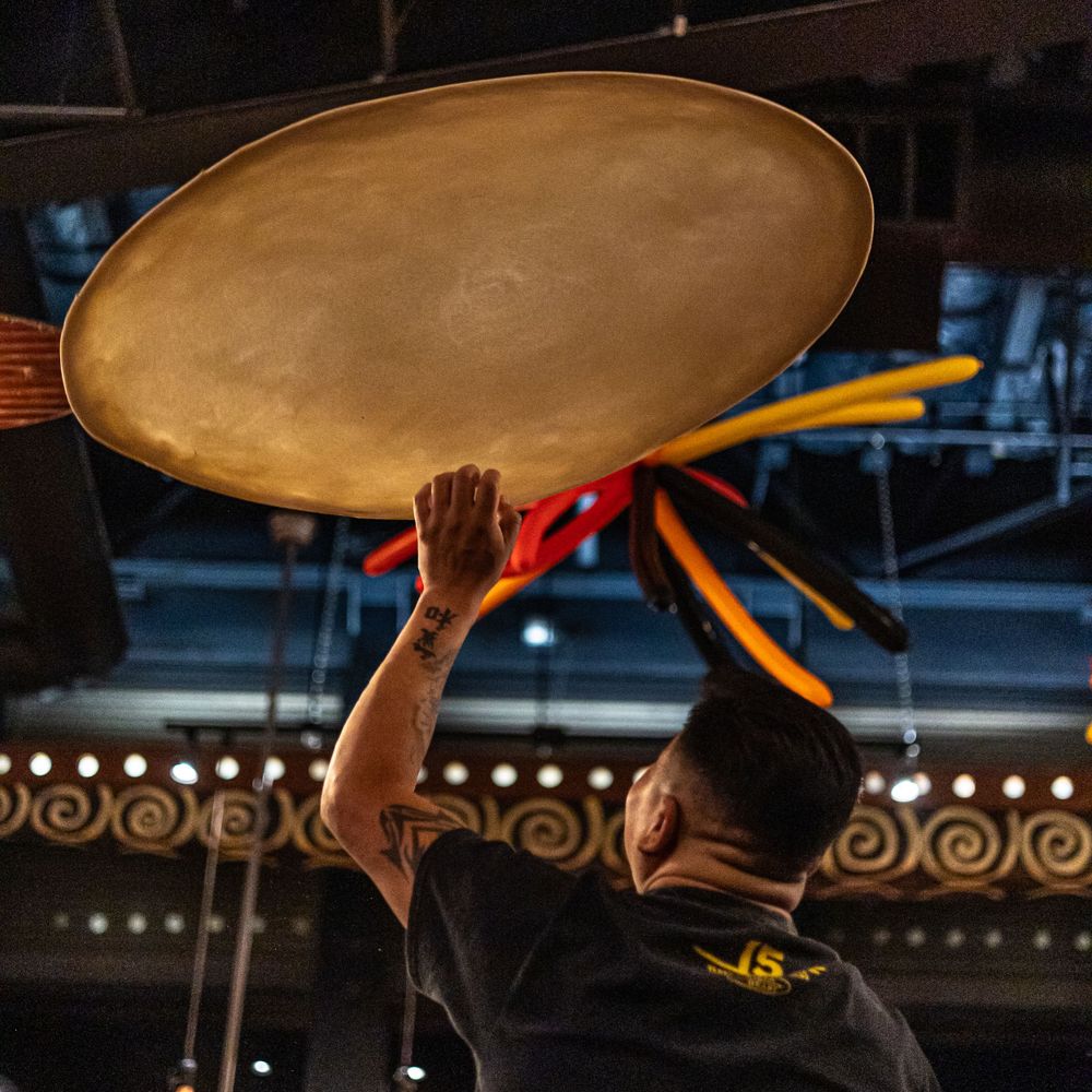 Pizza dough being tossed and spun in the air by a worker in a dimly lit restaurant.