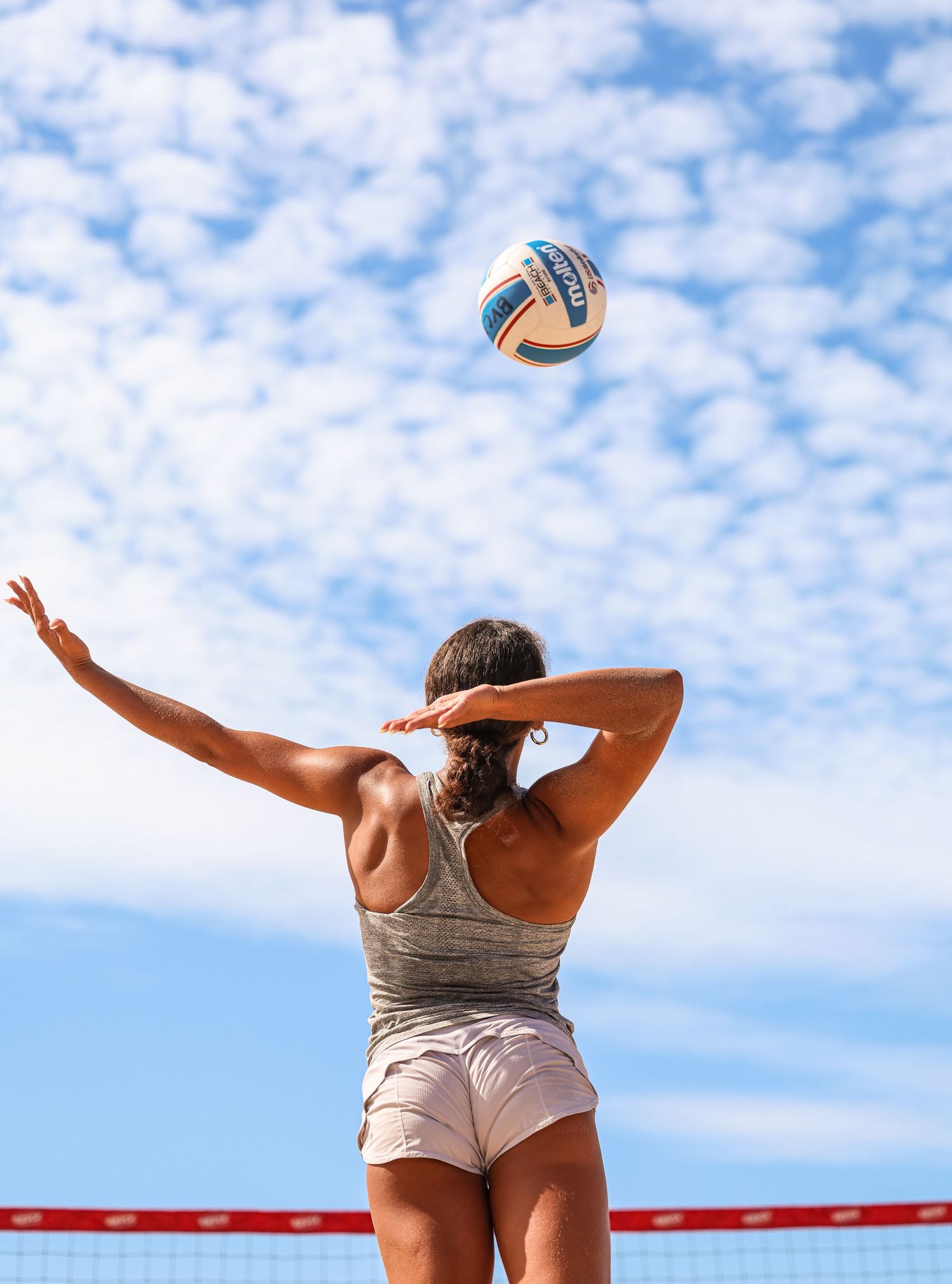 Beach volleyball player jumping near professional net against bright sky.