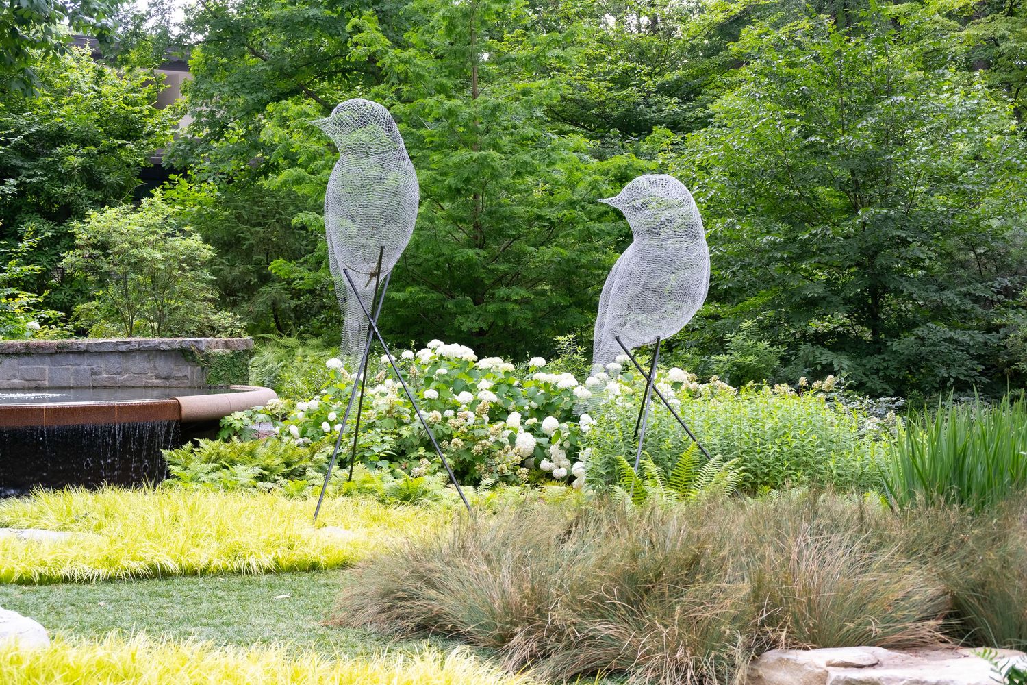 Two decorative glass bird sculptures displayed in a garden landscape.