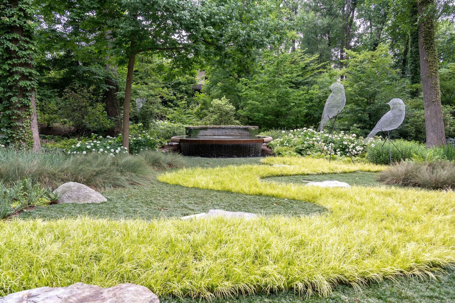Peaceful garden path with bridge and decorative rocks surrounded by yellow-tinted grass.