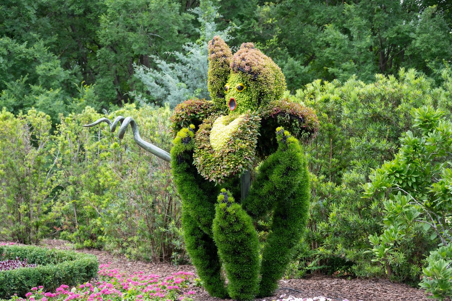 Large topiary sculpture with burgundy flower head and green leafy base in botanical garden.