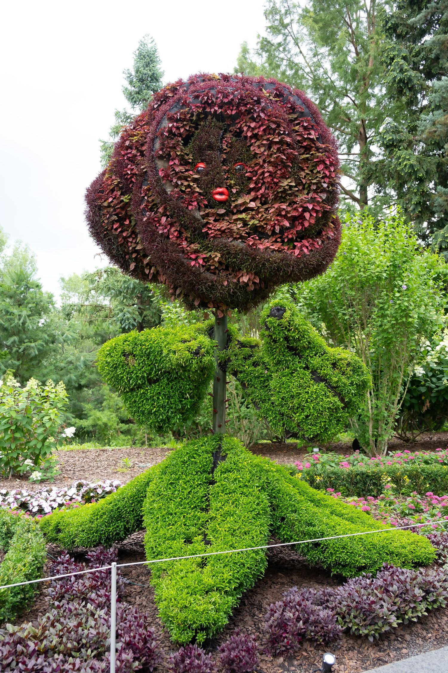 Whimsical topiary figure with green body and yellow accents in garden setting.