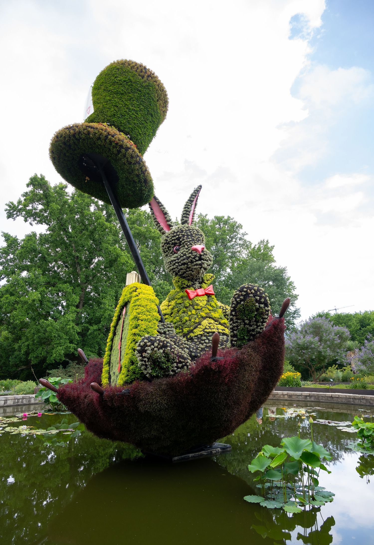 Elaborate topiary sculpture of a rabbit in a boat floating on a pond with decorative elements.