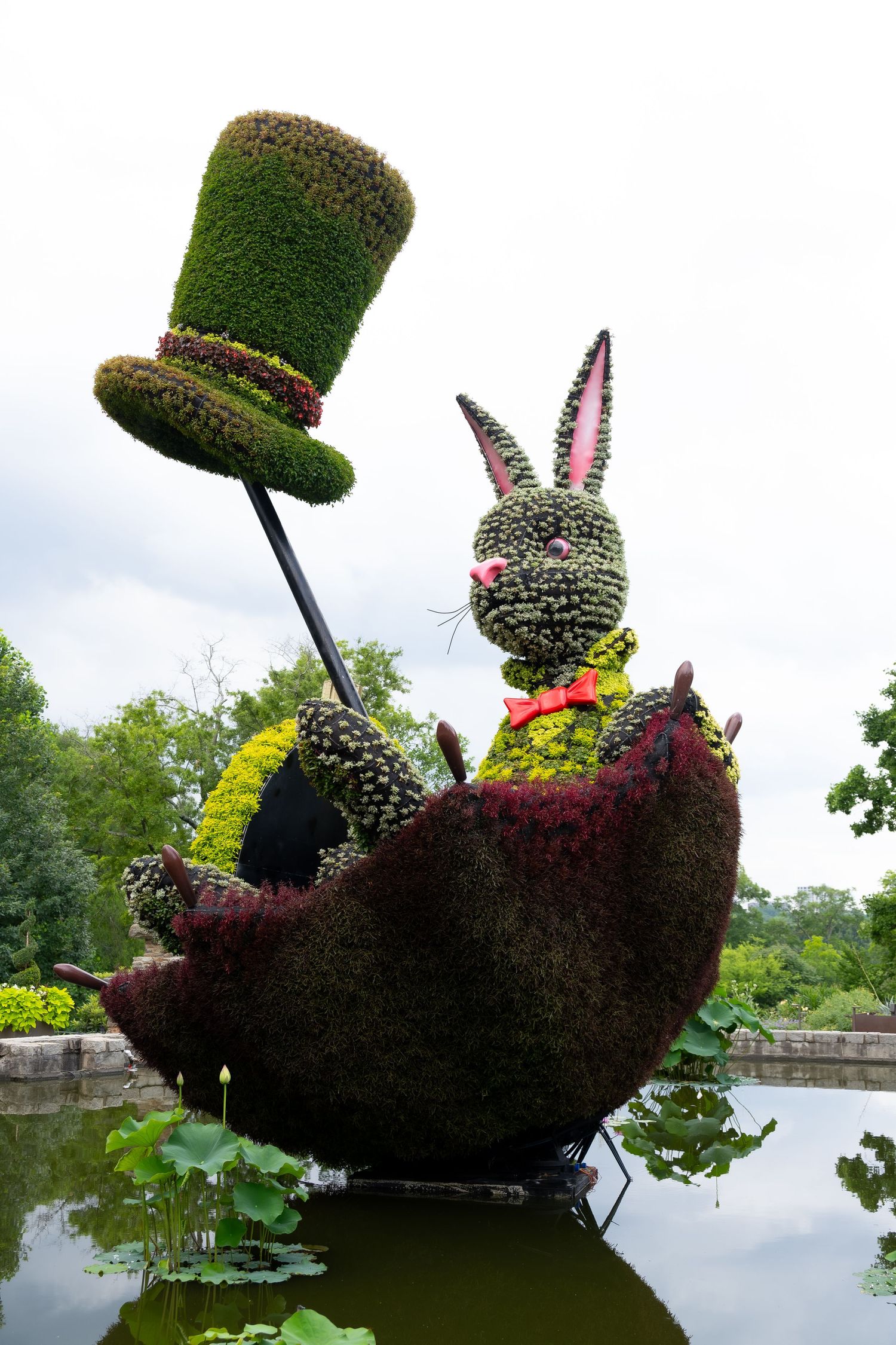 Garden sculpture showing a topiary rabbit in a boat with a tall green hat floating on water.