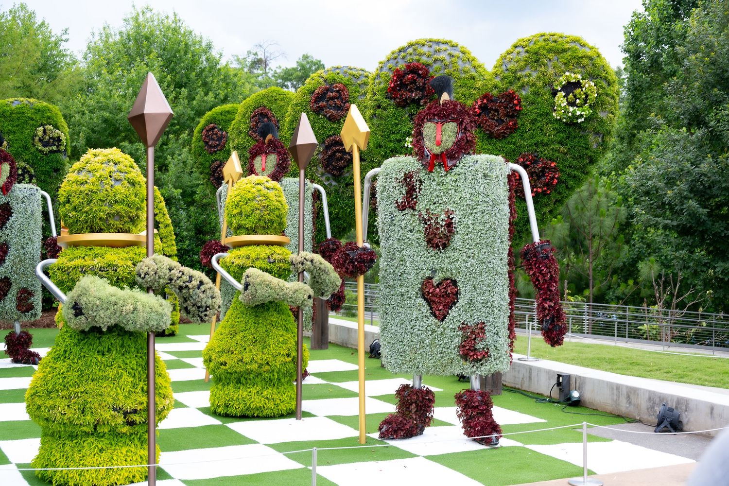 Topiary garden display featuring whimsical figures arranged on a checkered lawn path.