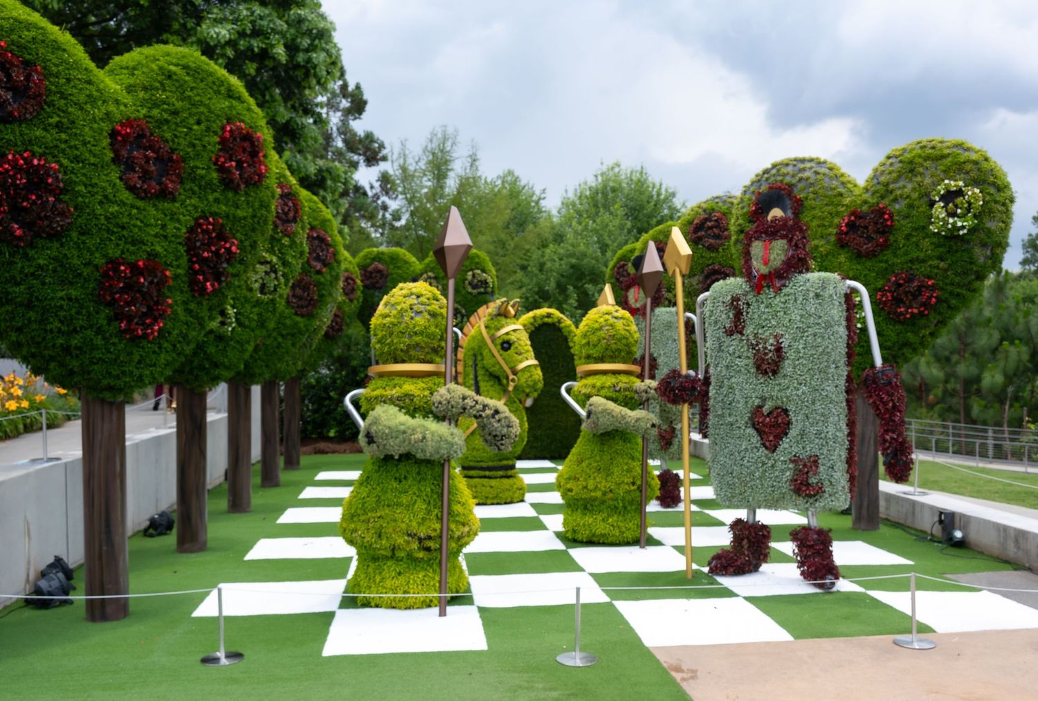 Wonderland-themed garden display with chess pieces and playing card topiaries on a green and white checkered lawn.