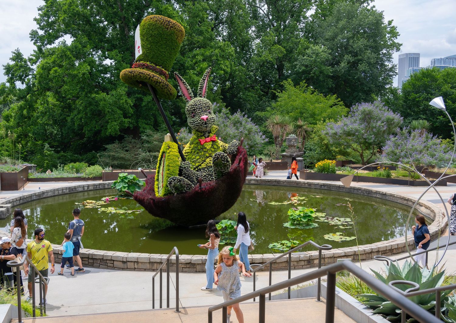 Whimsical topiary boat sculpture with rabbit character floating above a garden pond.