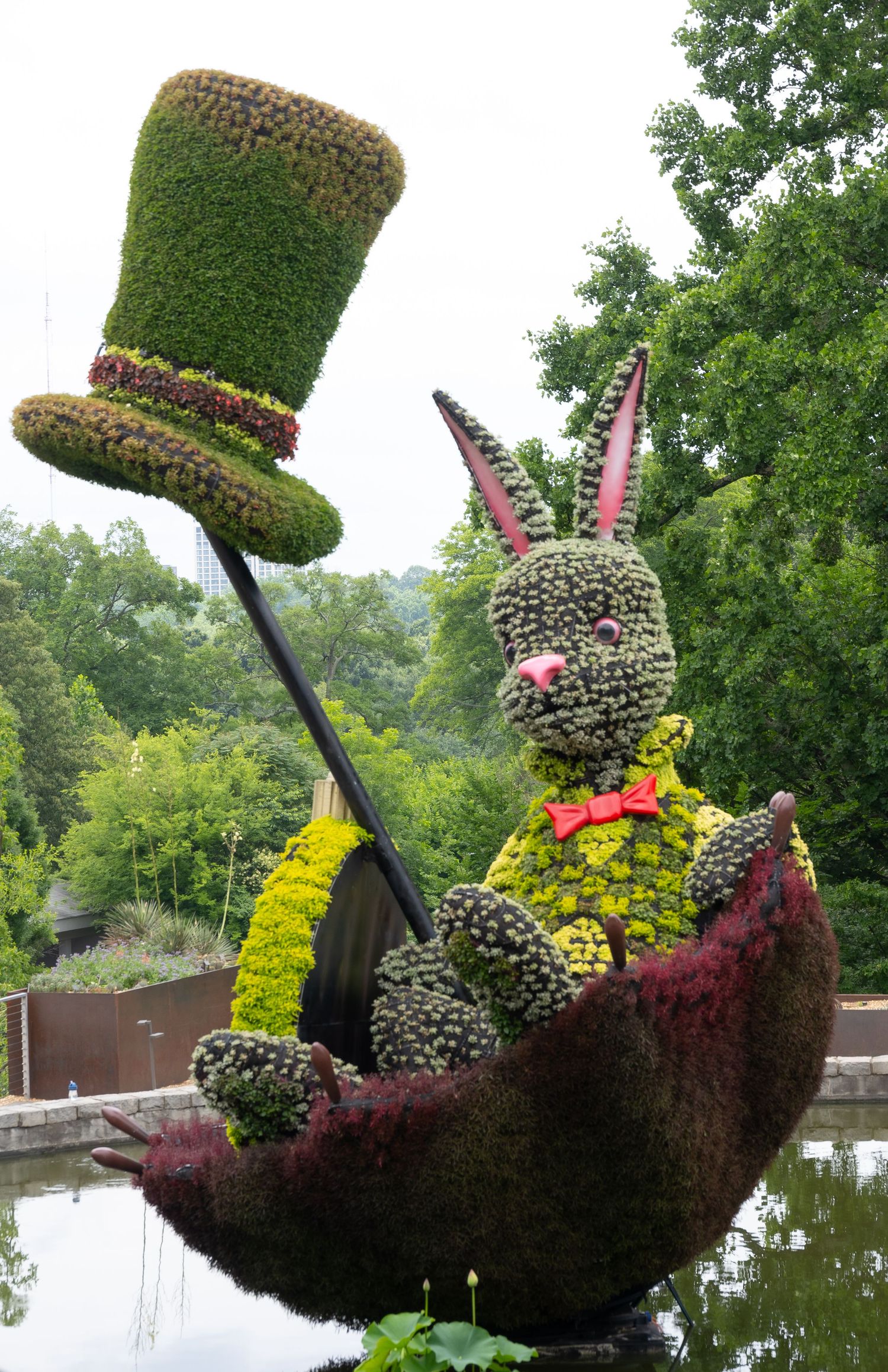 Large topiary rabbit in a boat wearing a top hat, created from green plants and flowers.