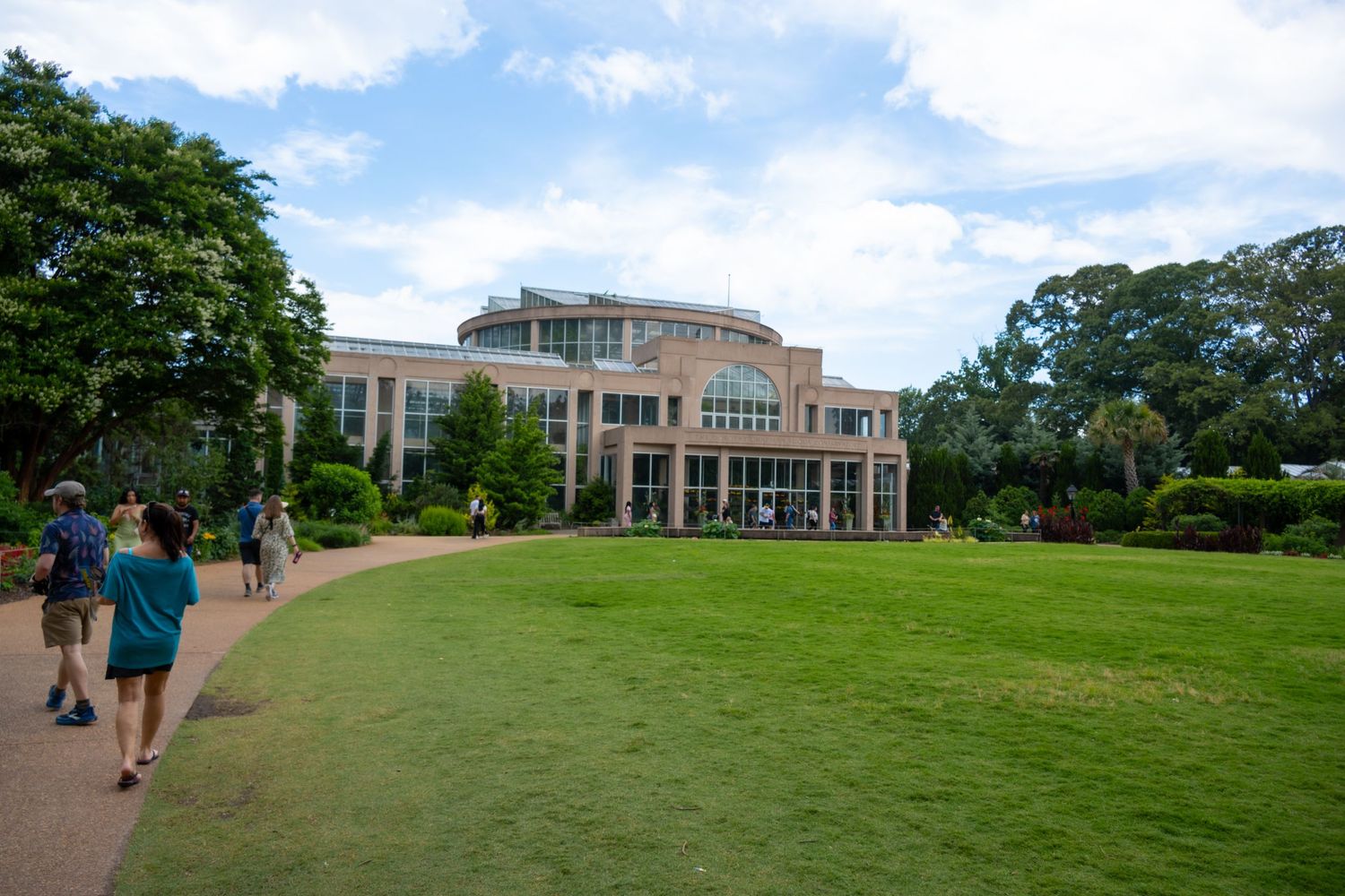 Modern glass building with manicured lawn and walking path under blue summer sky.