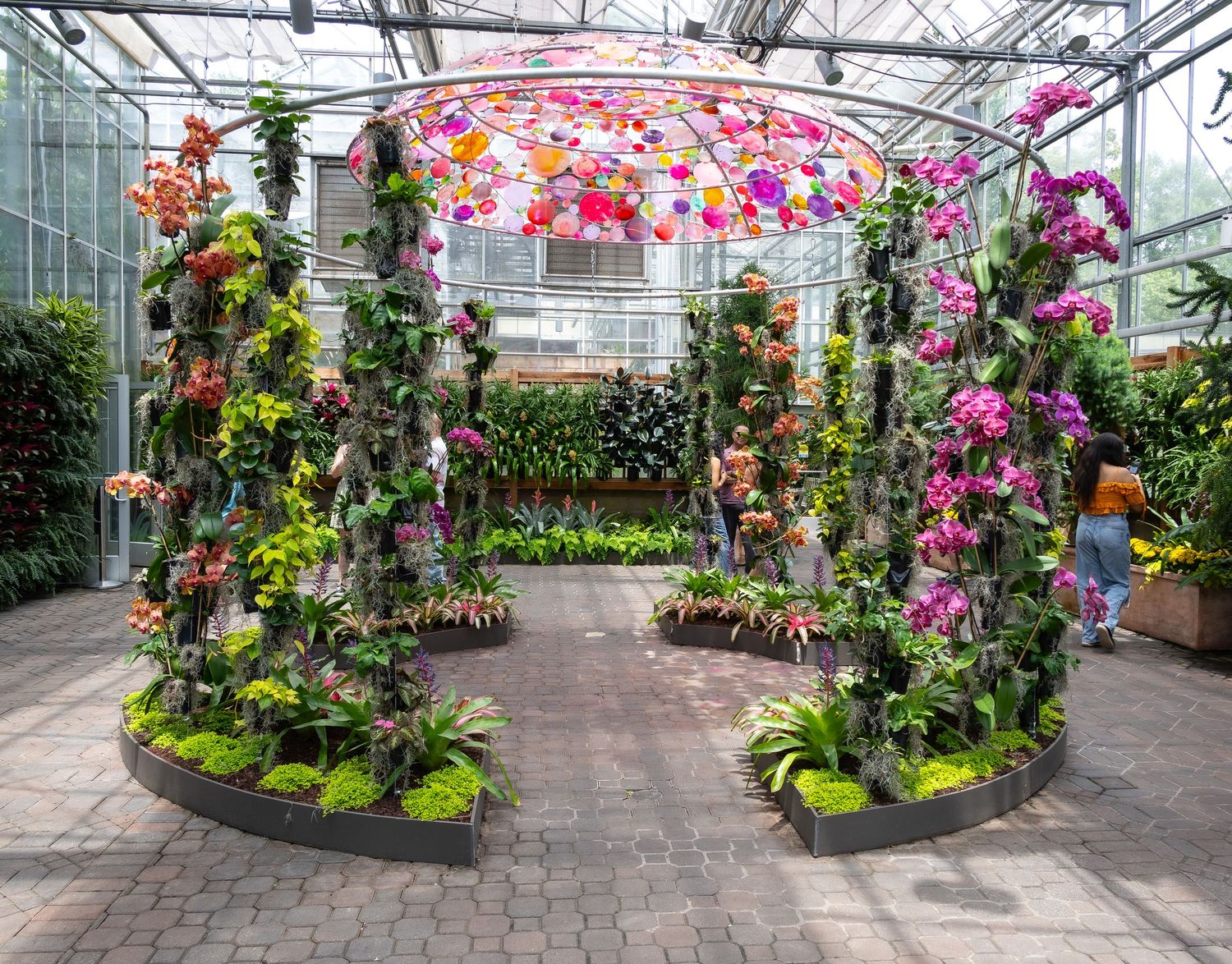 A greenhouse display features colorful orchids and tropical plants arranged in circular garden beds.