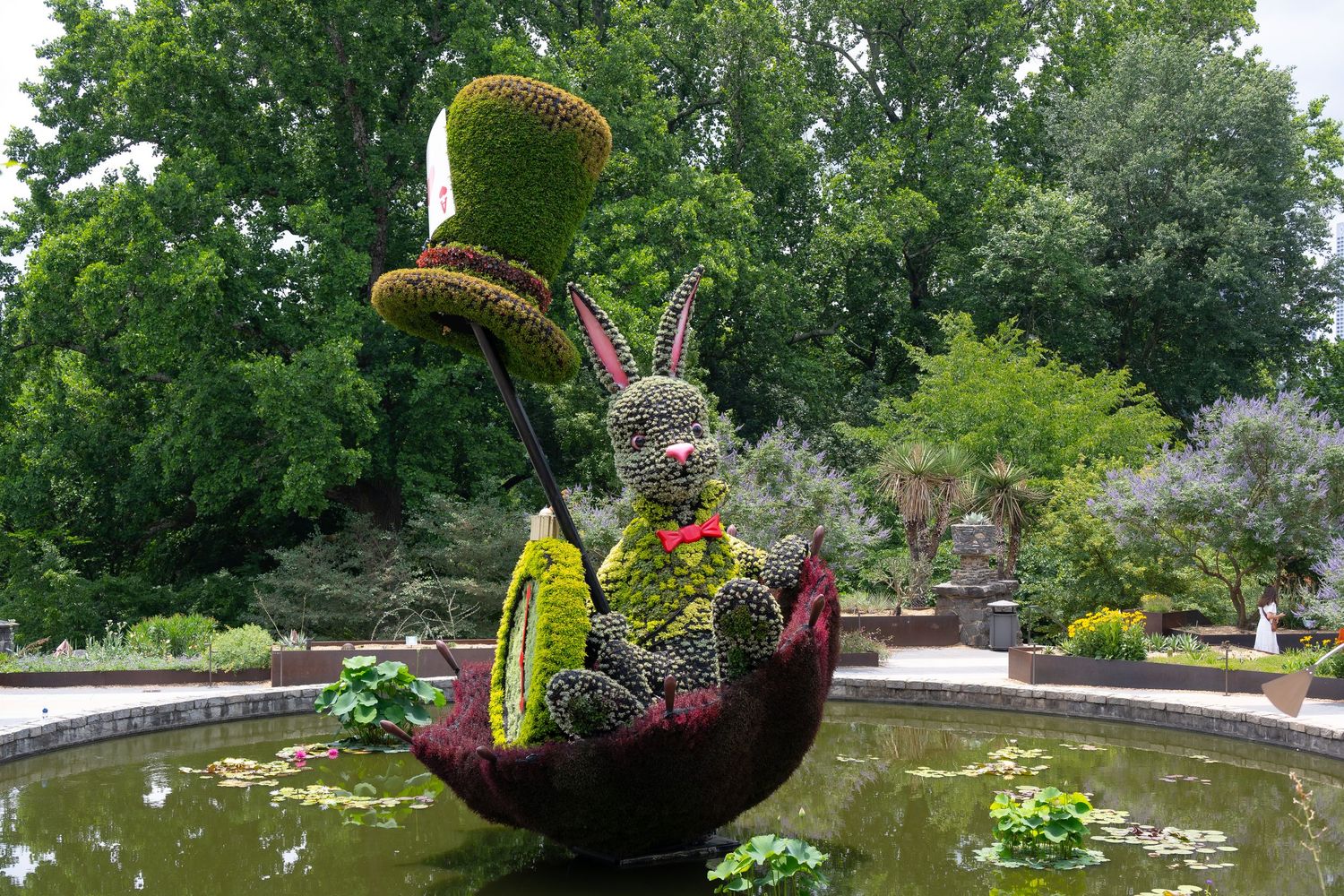 Creative topiary sculpture of a whimsical creature in a pond garden setting.