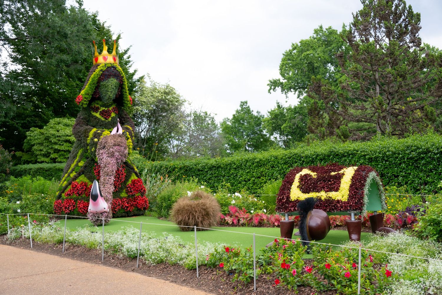 Large decorative garden display featuring a dragon-shaped topiary and ornate carriage on manicured lawn.