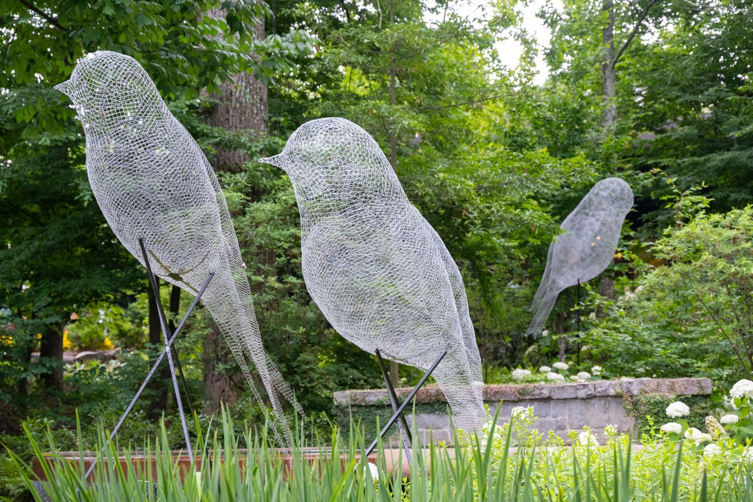 Wire mesh bird sculptures perched on poles in a garden setting.