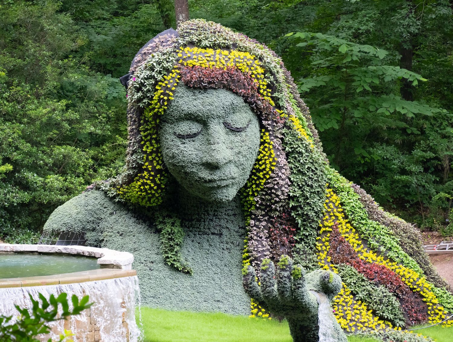 Large garden sculpture with colorful flowering plants creating a striking profile against lush greenery.