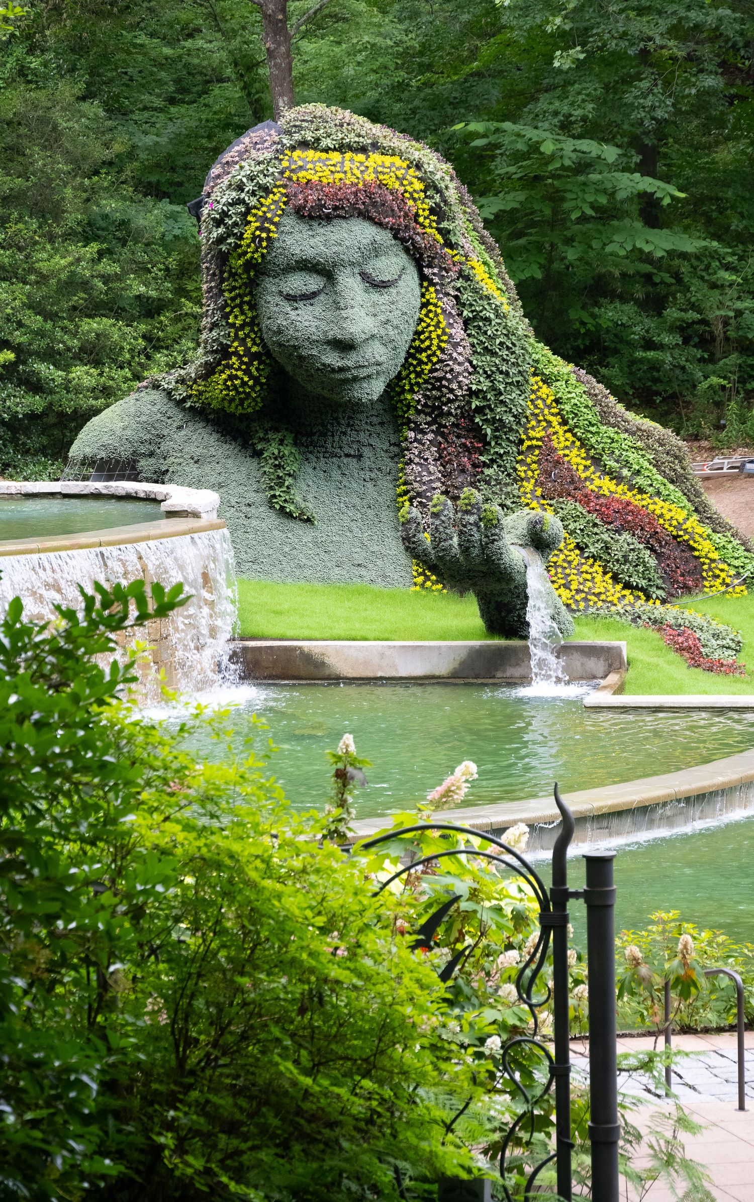 Impressive garden sculpture overlooking a peaceful water feature with flowering plants and stone paths.