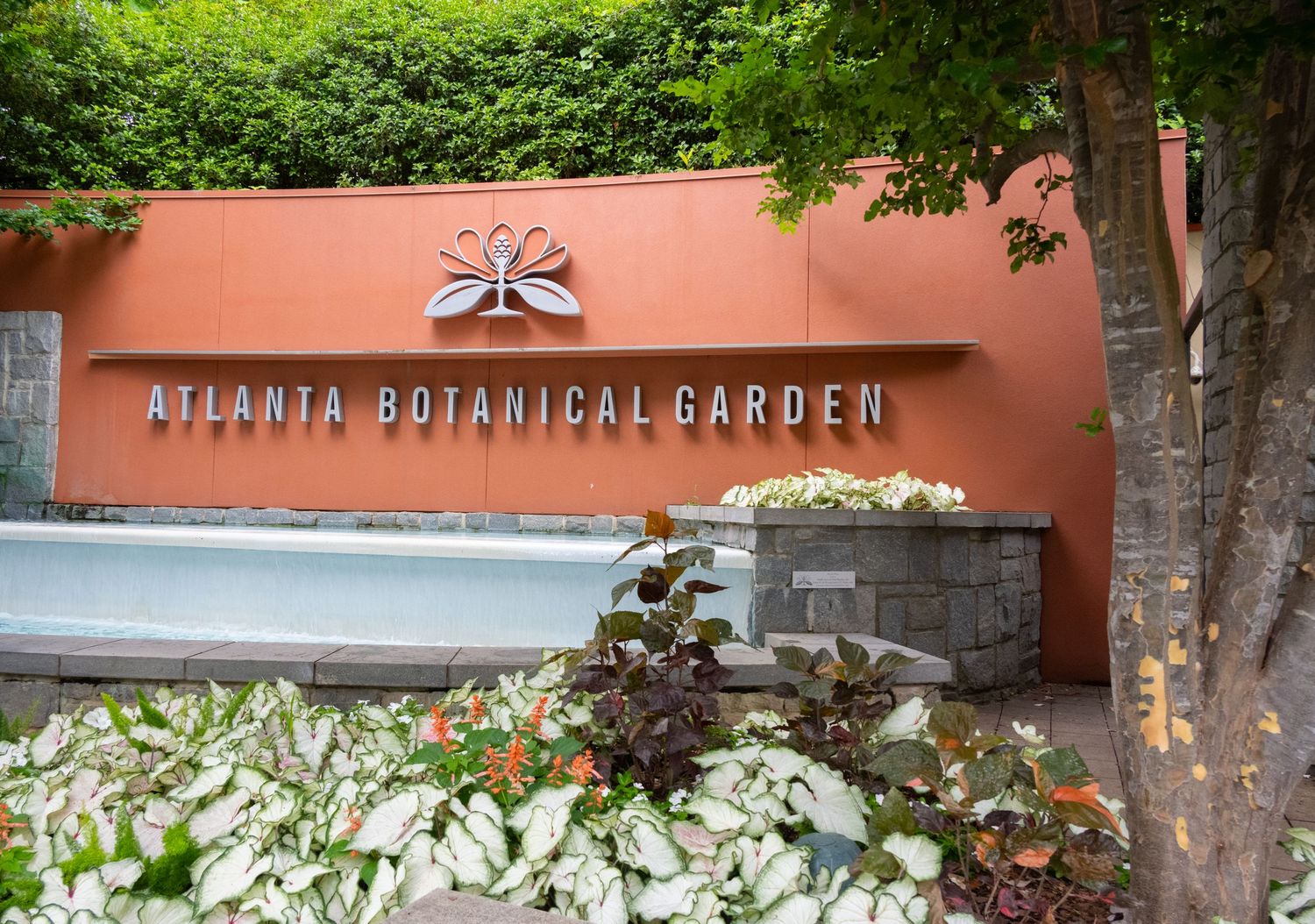 Entrance sign for the Atlanta Botanical Garden mounted on a terra cotta colored wall with landscaping.