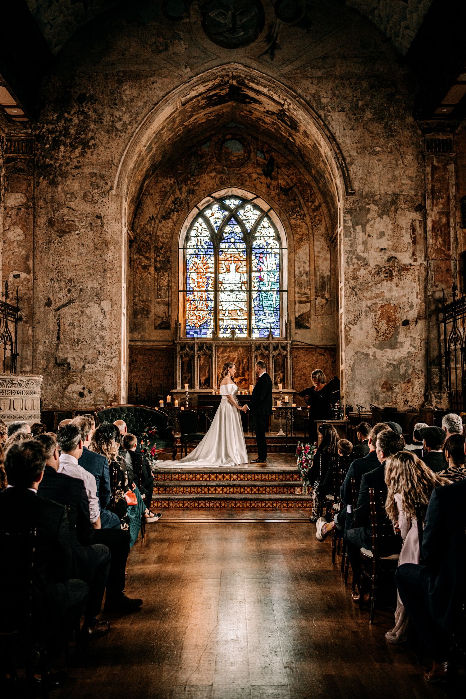 A traditional church wedding ceremony takes place in a historic stone chapel with stained glass windows and gathered guests.