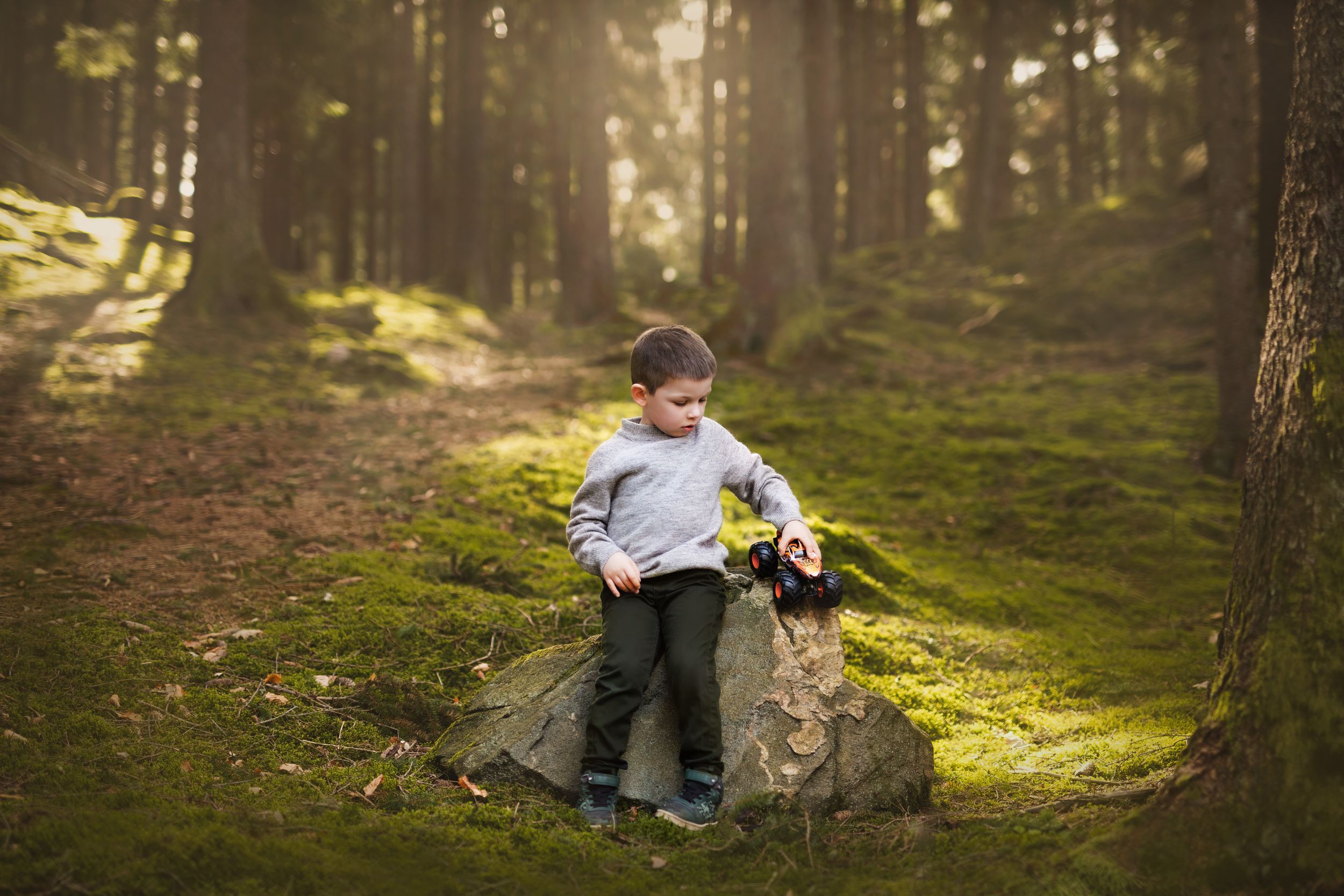 En pojke i skogen sitter på en sten och leker med sin leksak.