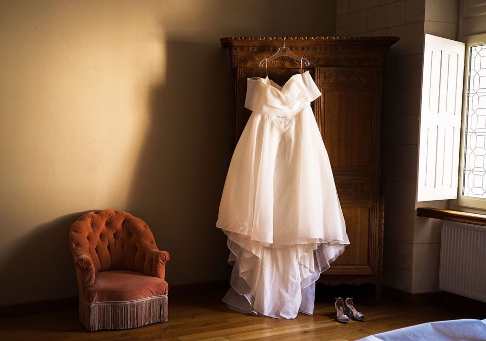 White wedding dress hanging in a sunlit room with vintage furniture.