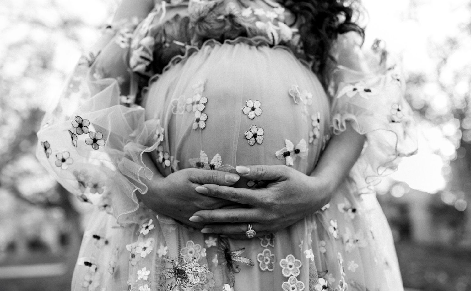 Black and white photo of a pregnant woman in a floral dress holding her baby bump.