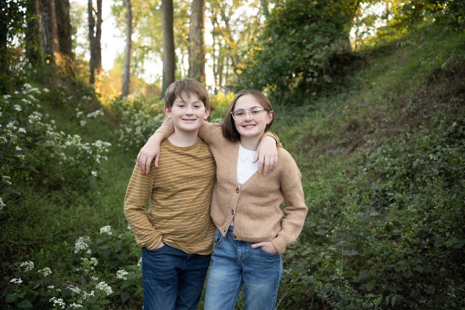 Two people in tan sweaters smiling together on wooded path.