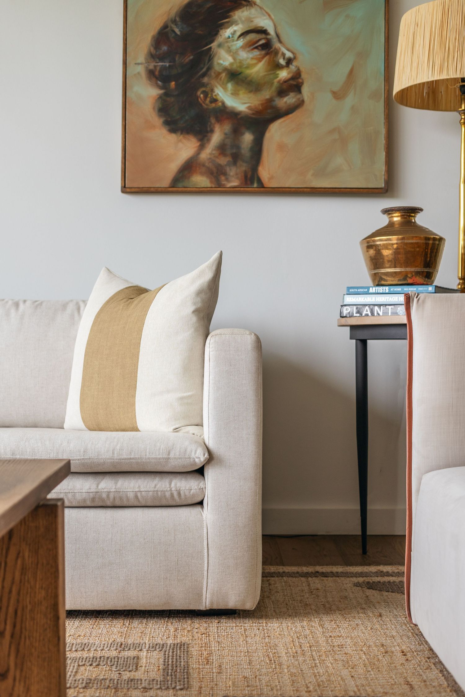 Modern living room corner with beige sofa, portrait art, and brass table lamp.