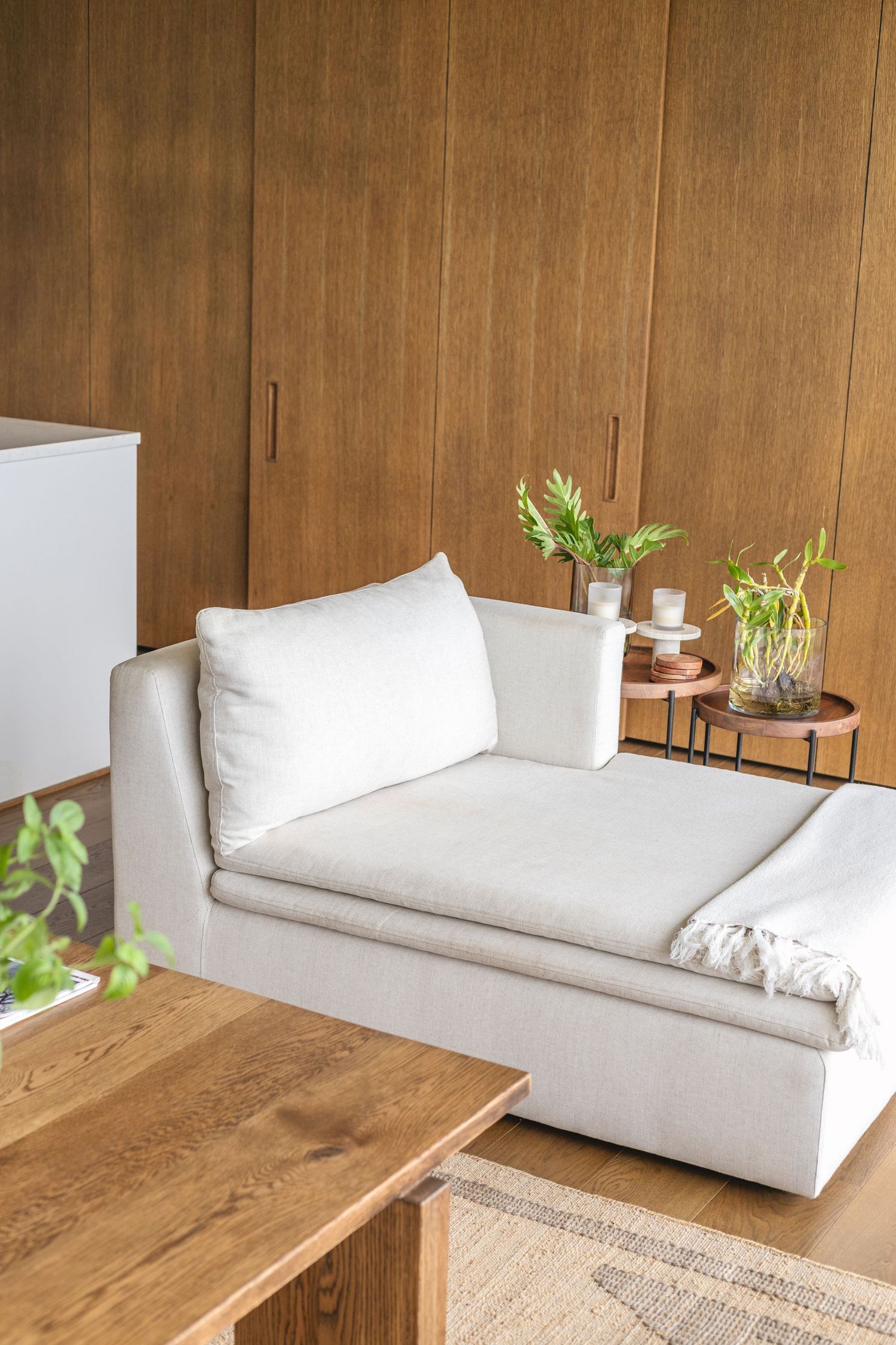 Modern minimalist living room with white couch and wooden accent furniture.