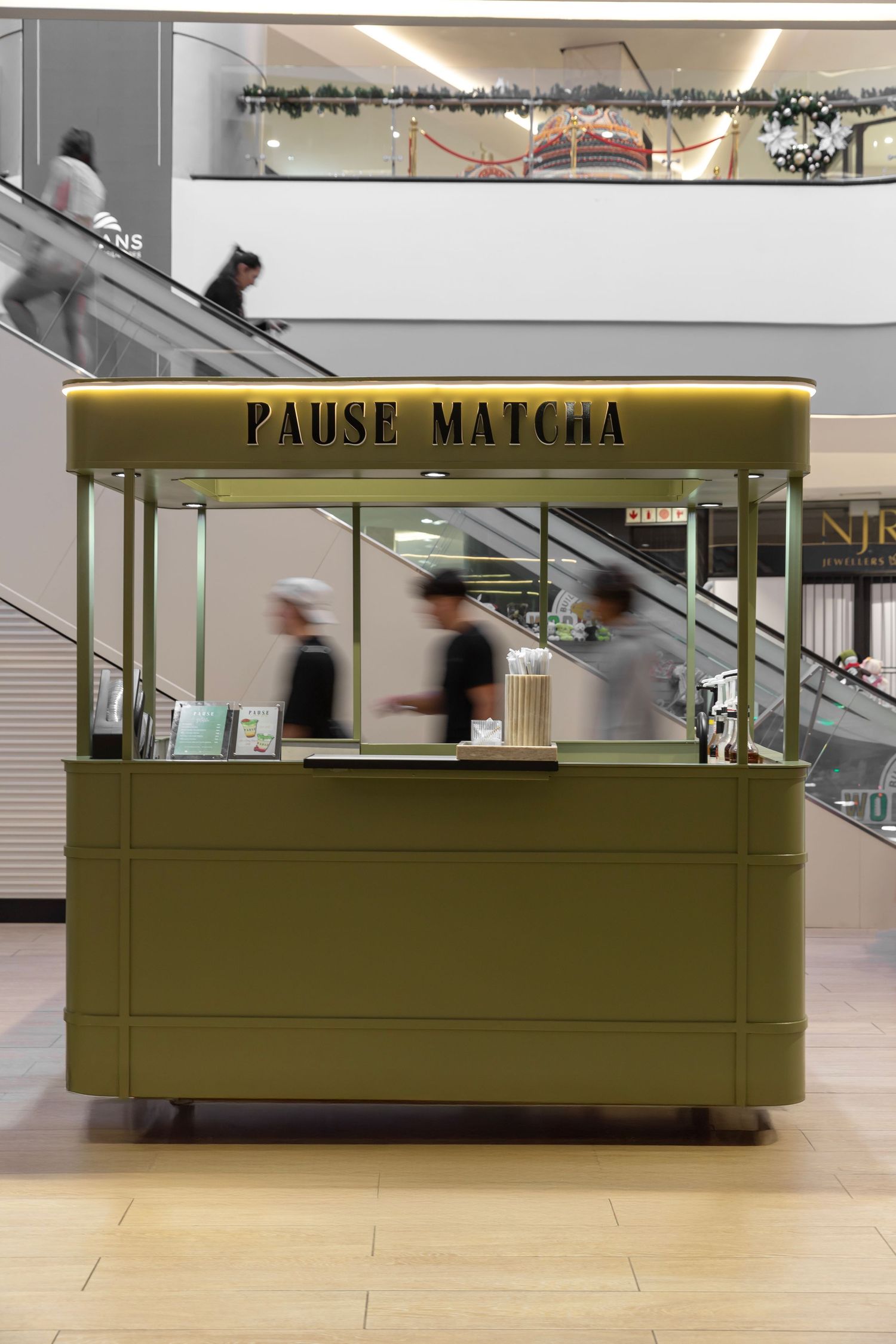 Modern olive green matcha cafe kiosk with clean minimalist design in a bright shopping mall interior.