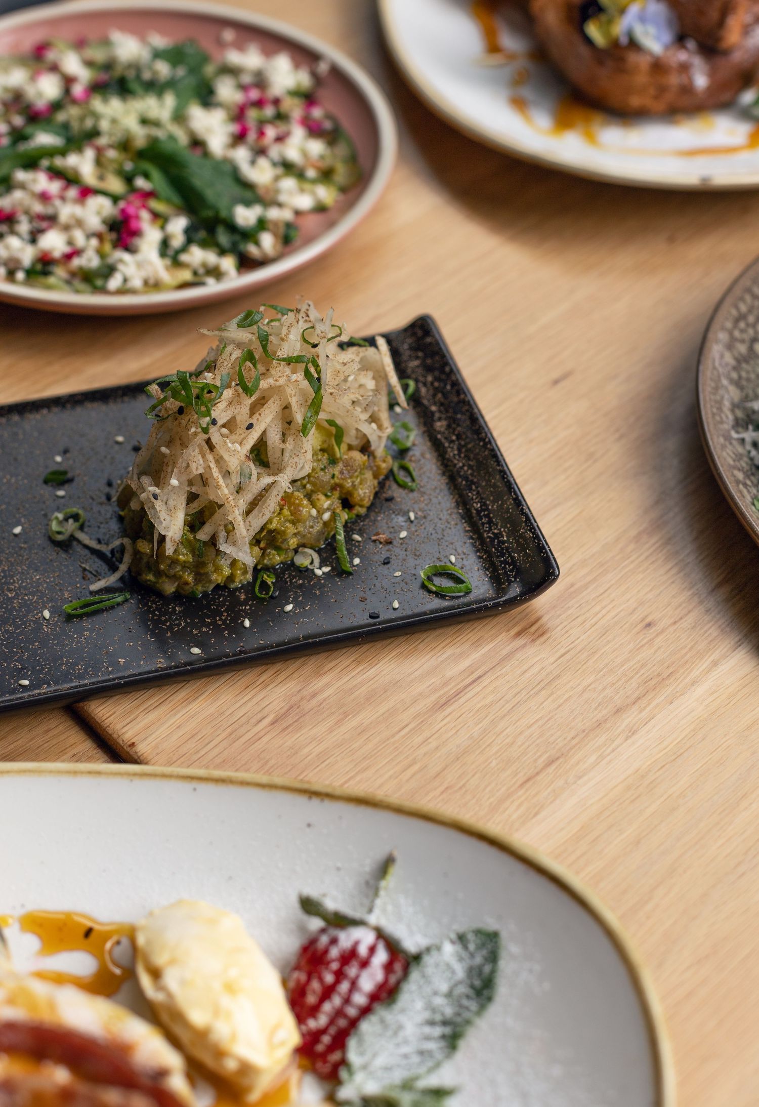 Various gourmet dishes on plates including a salad and topped noodle dish.