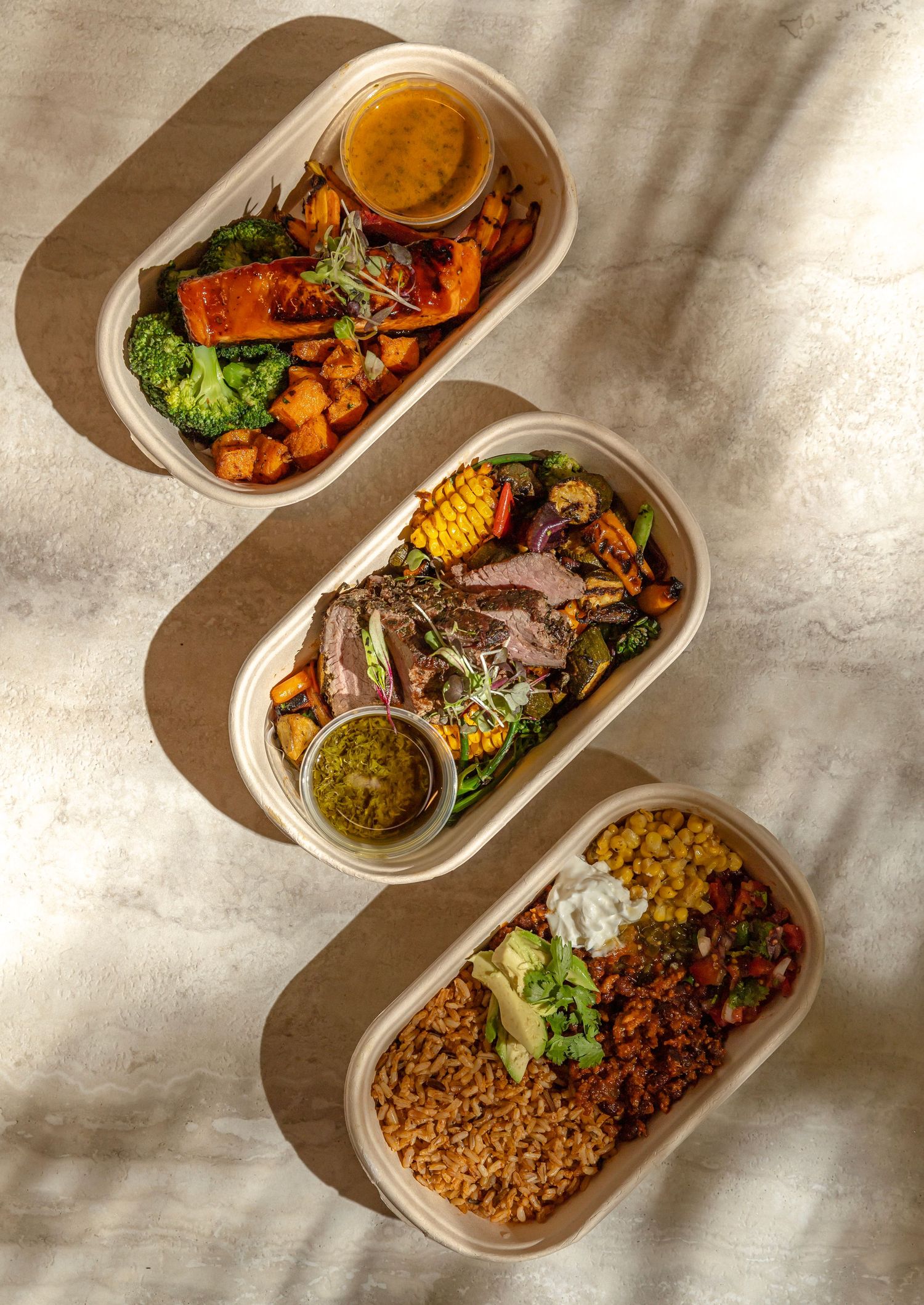 Three eco-friendly takeout containers filled with colorful healthy meals including roasted vegetables, grilled meats, and rice bowls.