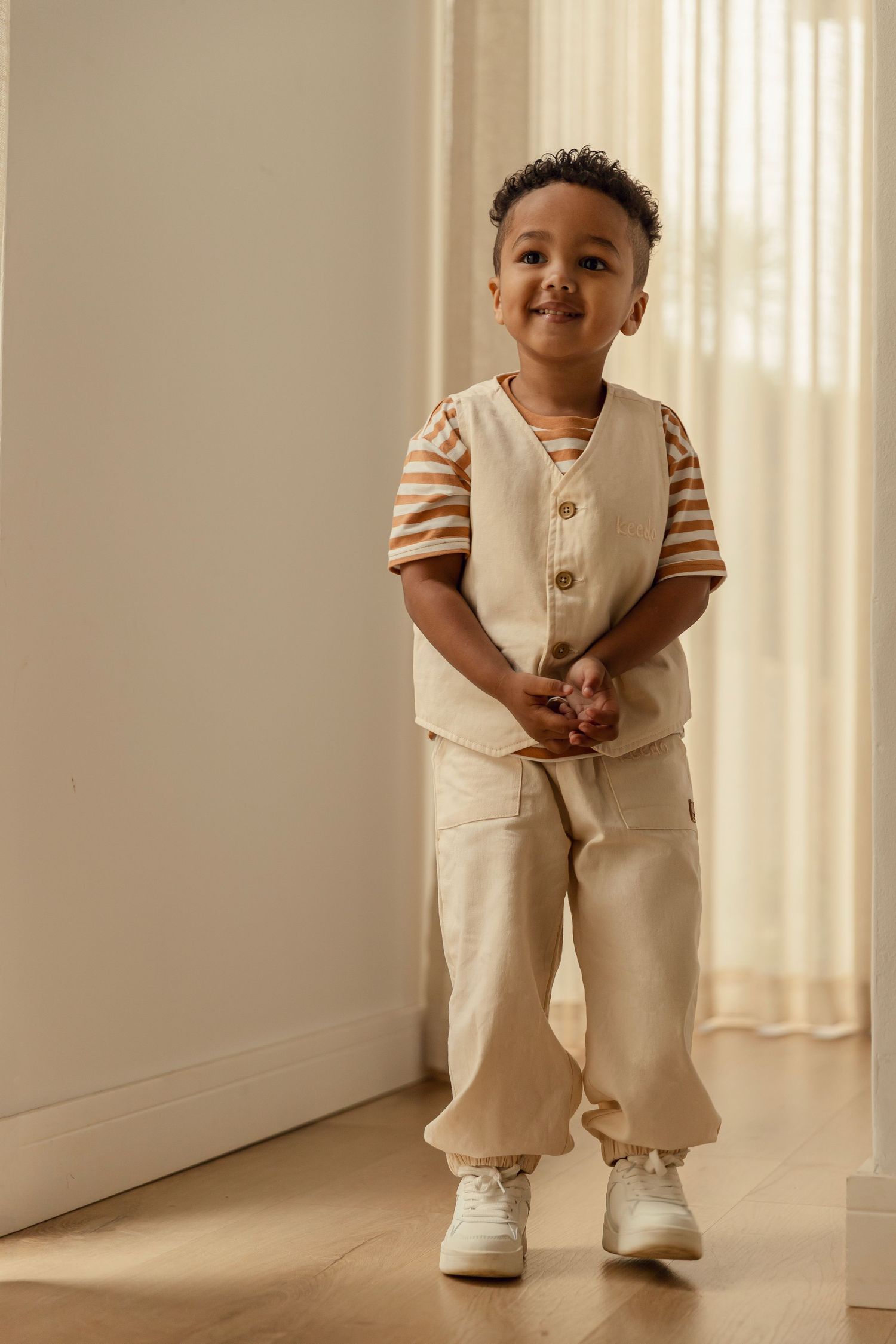 A series of four photos showing a toddler in cream-colored clothing and white shoes standing against a light background.