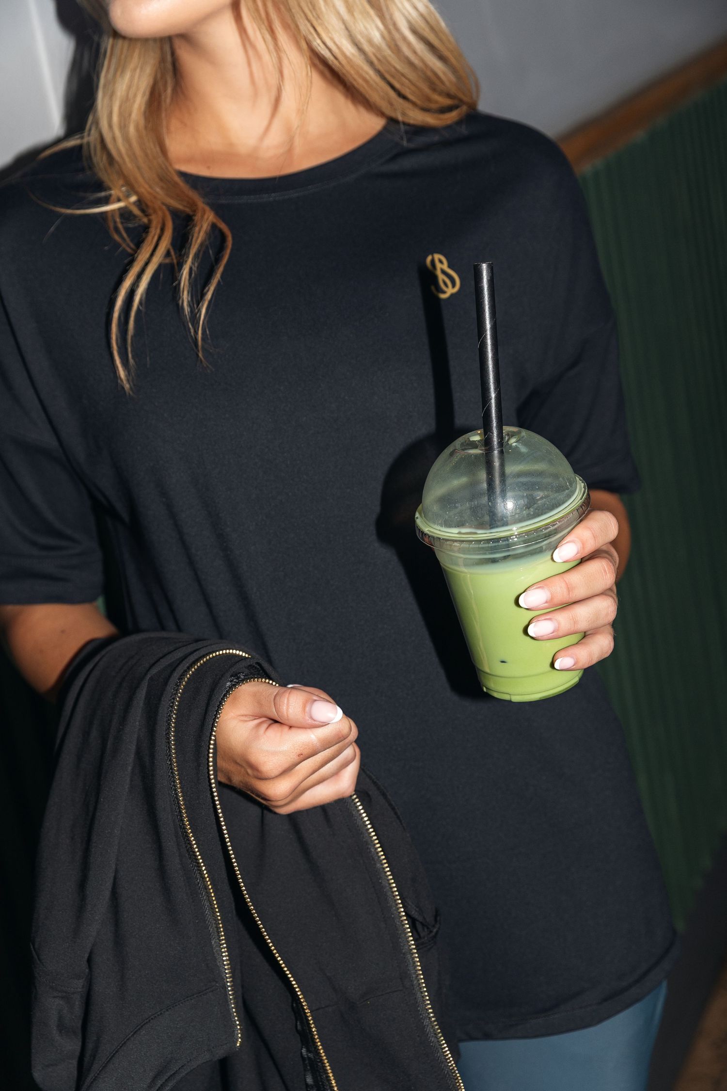 Person in a black shirt holding a green smoothie drink with a reusable straw.