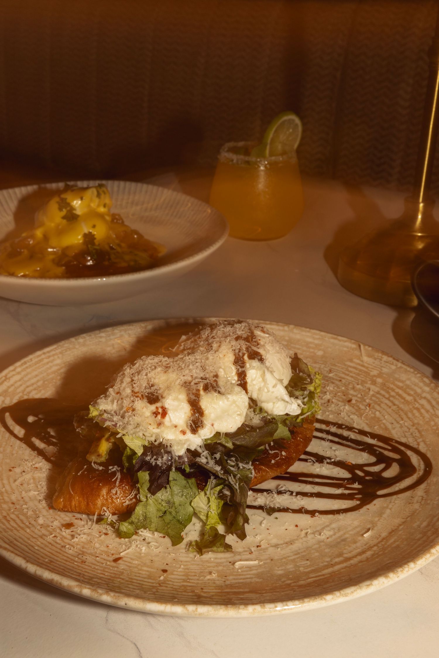 Elegant restaurant dish featuring grilled food topped with burrata and shaved parmesan on a rustic plate with balsamic drizzle.