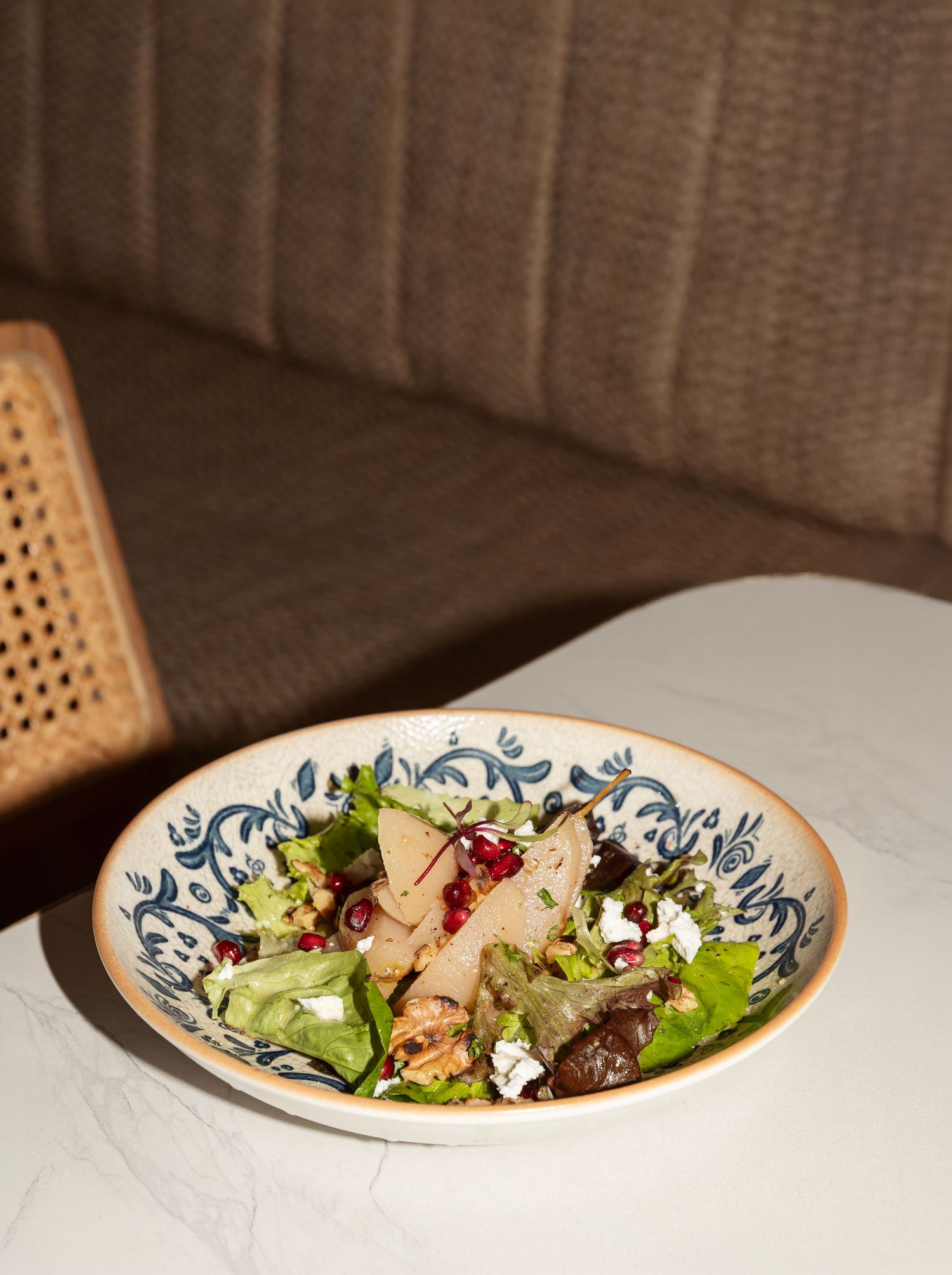 A decorative blue and white bowl filled with fresh salad, pomegranate seeds, and feta cheese on a marble table.