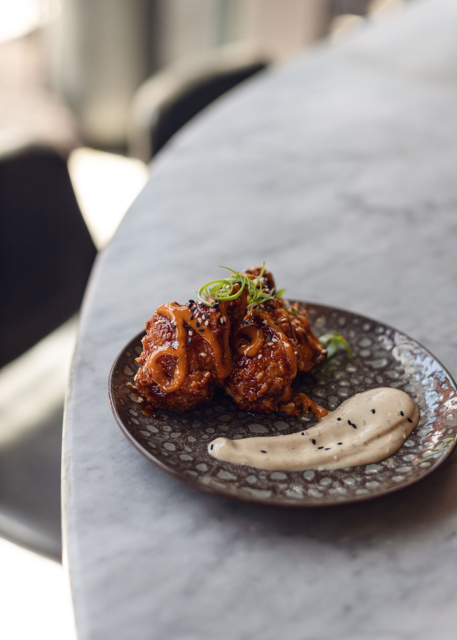 Glazed chicken wings served on textured plate with creamy sauce.