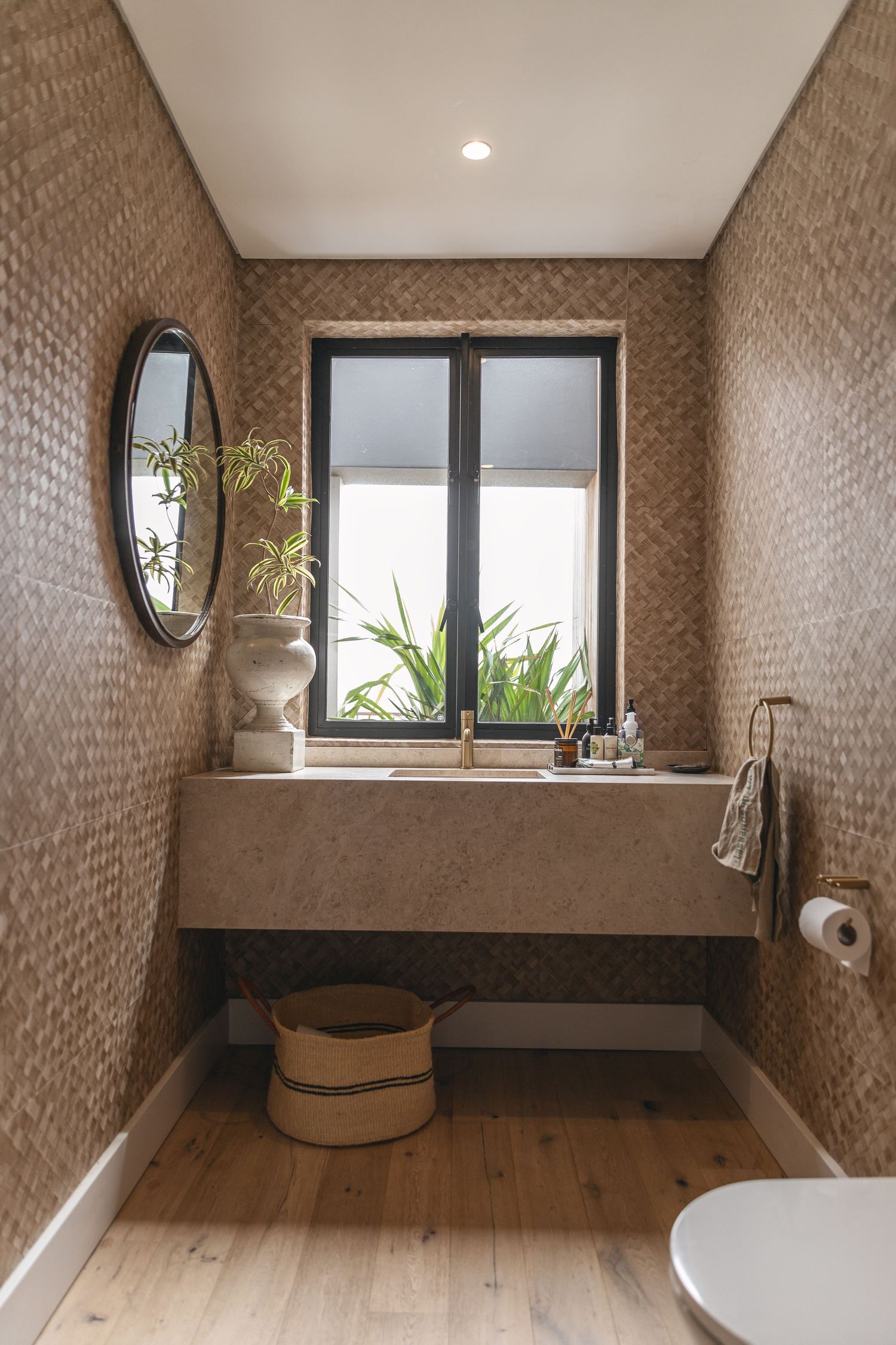 Modern bathroom interior with textured brown walls, oval mirror, minimalist concrete sink, and wooden floor details.