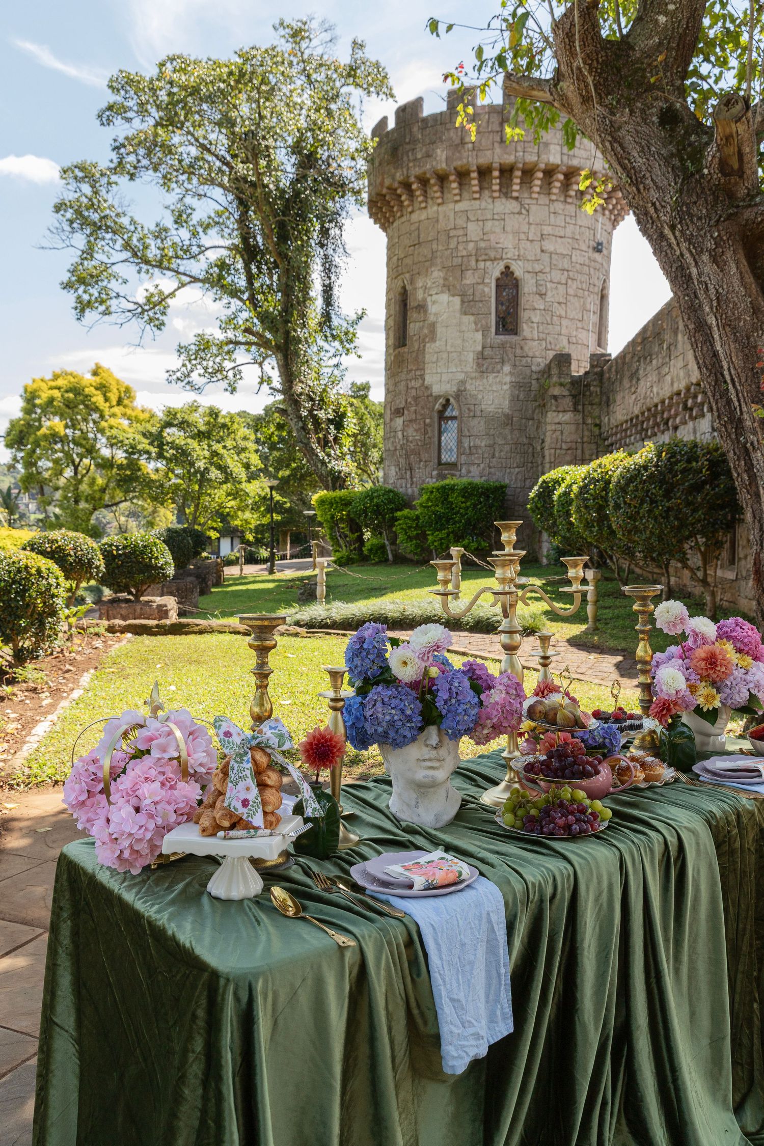 Elegant outdoor table with colorful flowers and candles set in a lush garden beside a medieval stone castle tower.