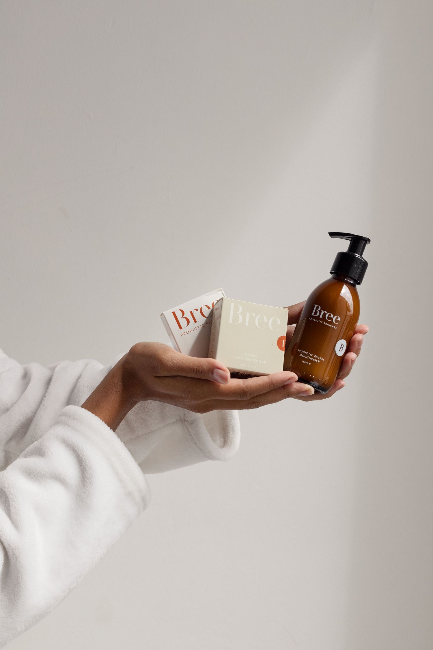 Hands holding beauty products against white background with amber bottle and white packaging.