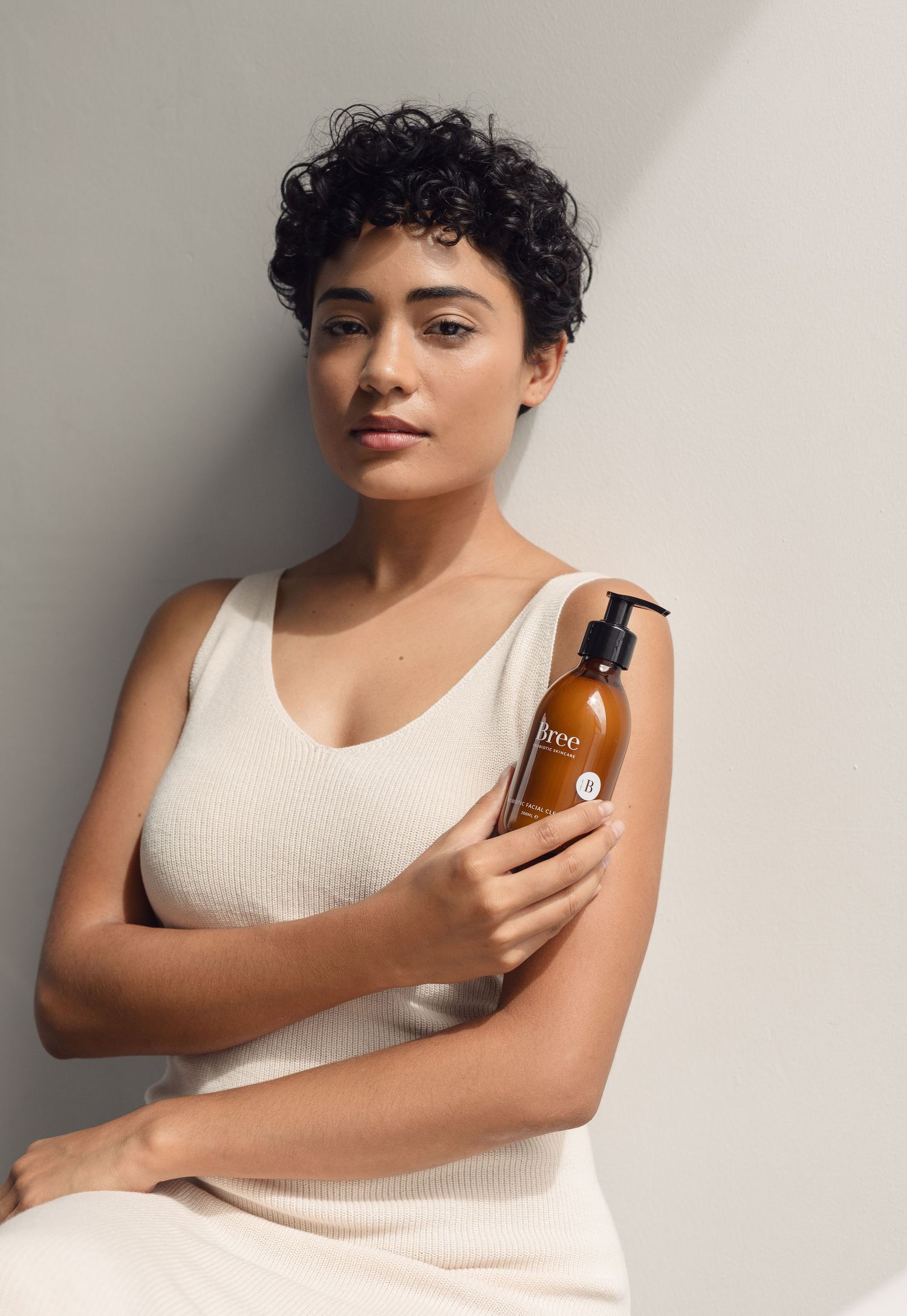 Beauty product advertisement featuring model in white tank top holding amber bottle.