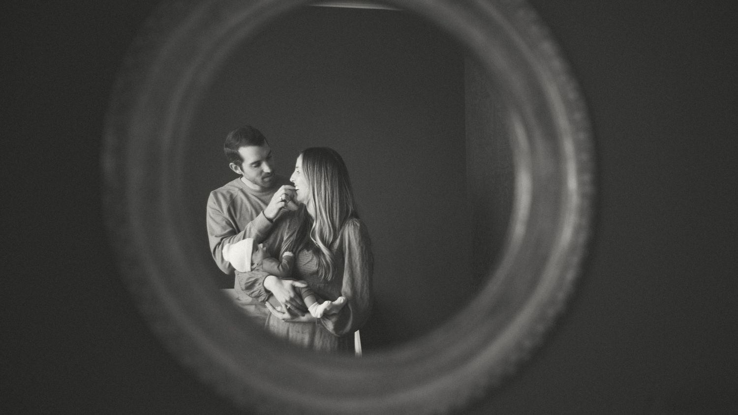 Artistic black and white portrait through circular frame showing tender moment.