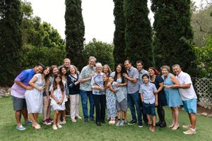 Group of family members leaning in together smiling. They are wearing different shades of blue, standing in front of a green background.