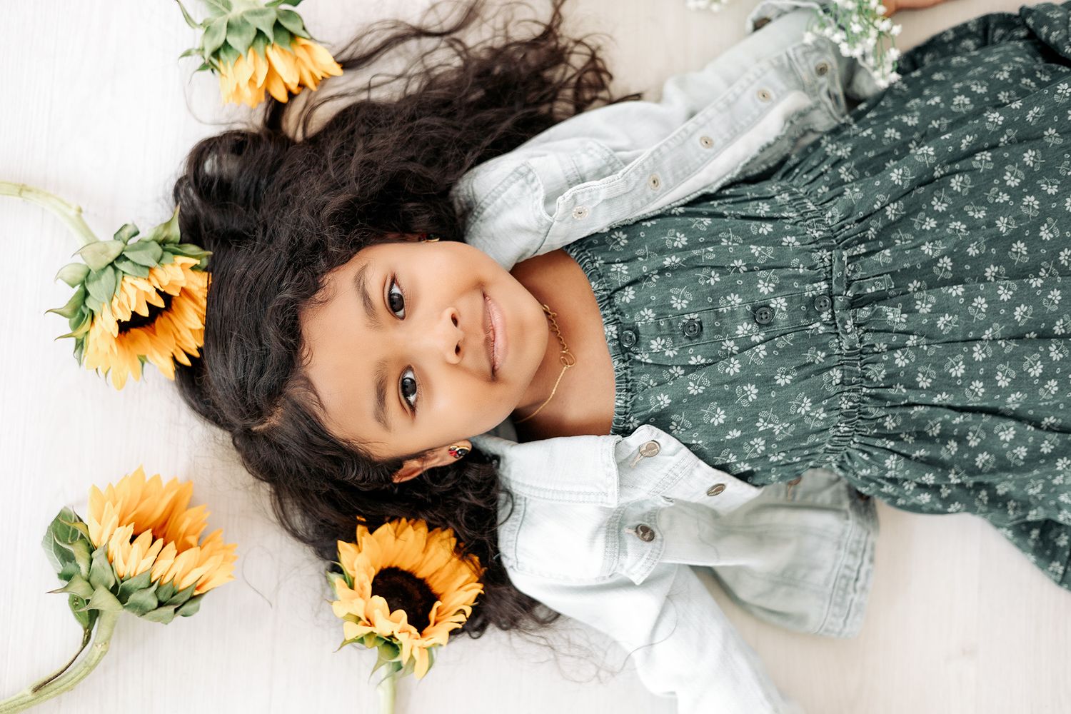 Artistic portrait session with sunflowers and green floral dress against white background.