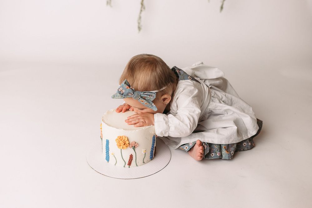 Professional photo of a toddler in white smashing a cake