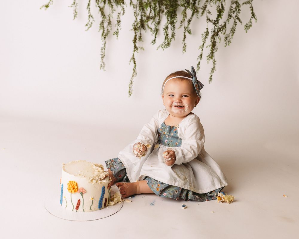 Professional photo of a toddler in white smashing a cake
