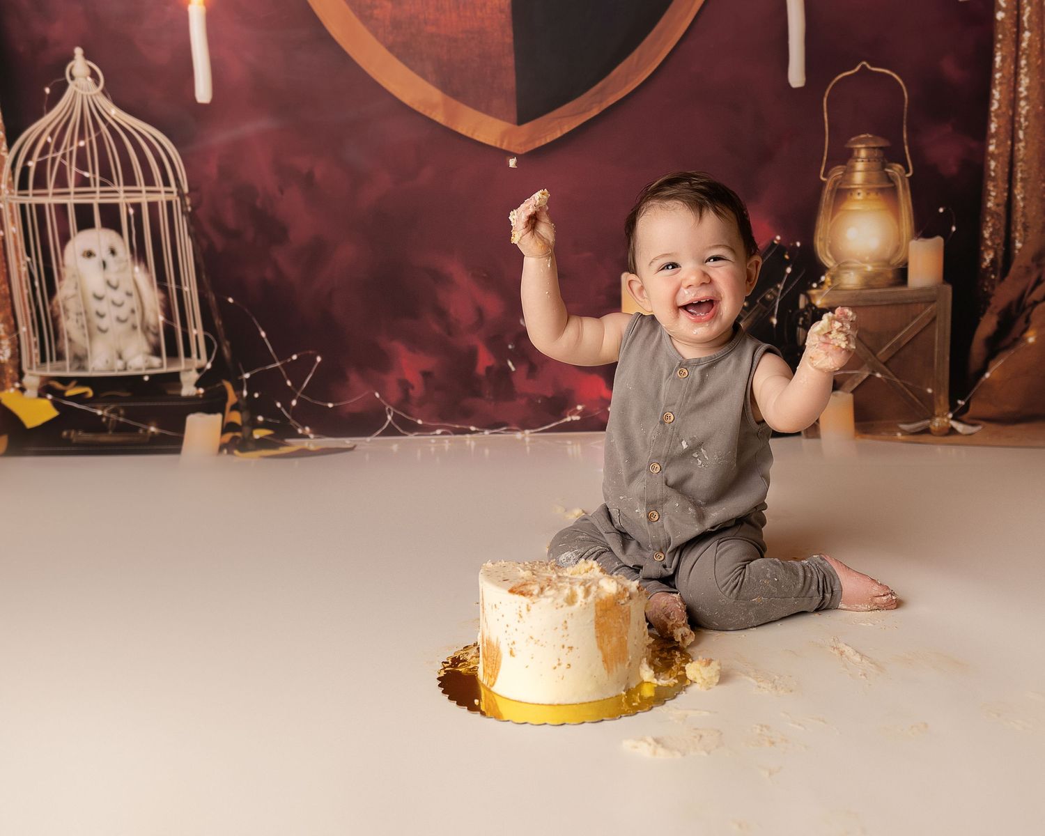 Professional photo of a toddler in brown in front of a Harry Potter themed back drop smashing a cake