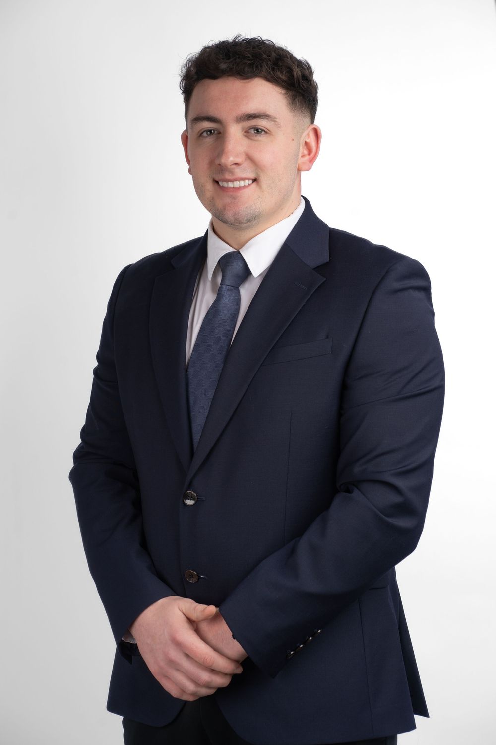 Professional headshot portrait of someone in a dark navy suit and tie against a crisp white studio background.