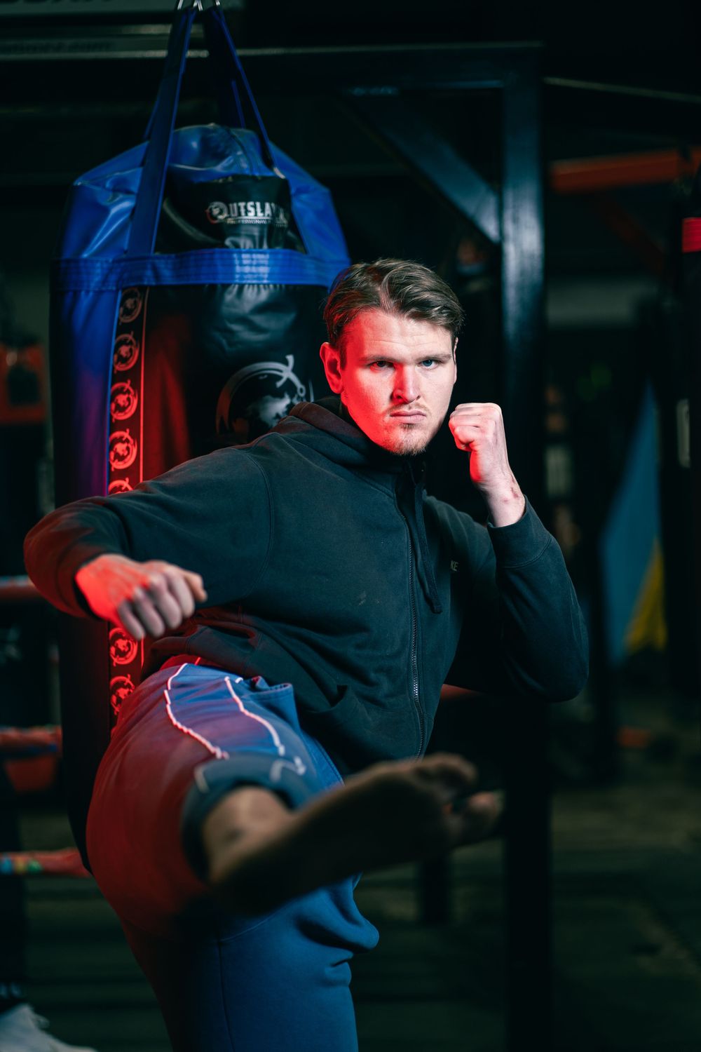 Boxer training with red heavy bag in dark gym during intense workout session with dramatic lighting.