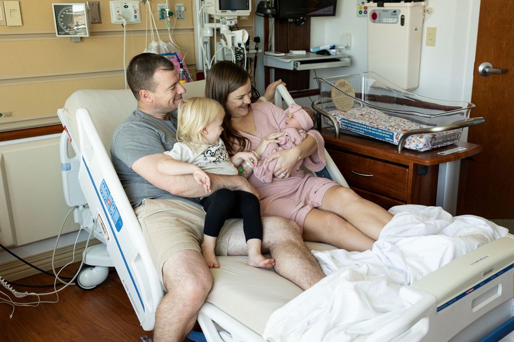 Hospital room with medical equipment and family members gathered around bed.