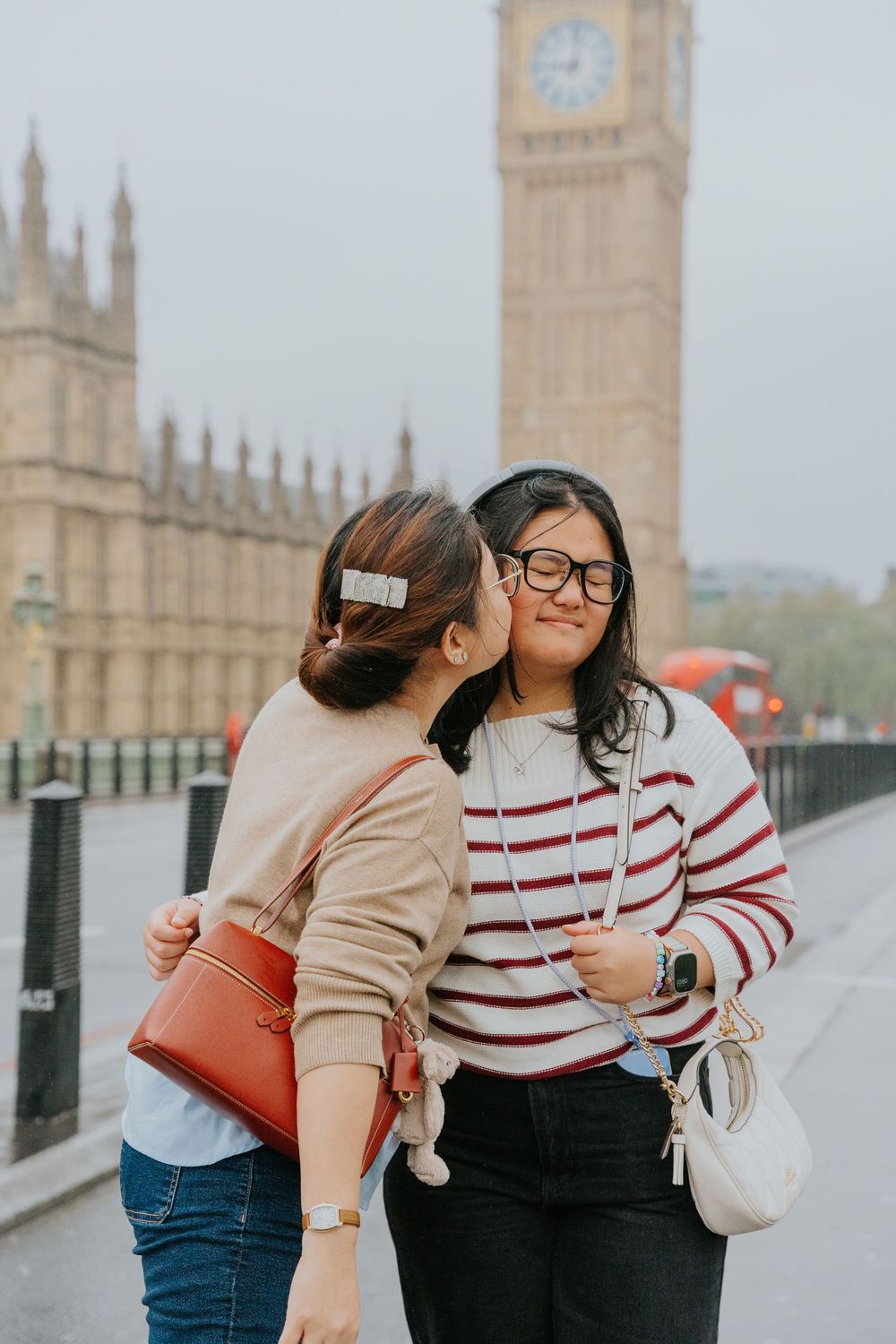 Two people embrace and laugh together on Westminster Bridge with the Houses of Parliament visible in the background.