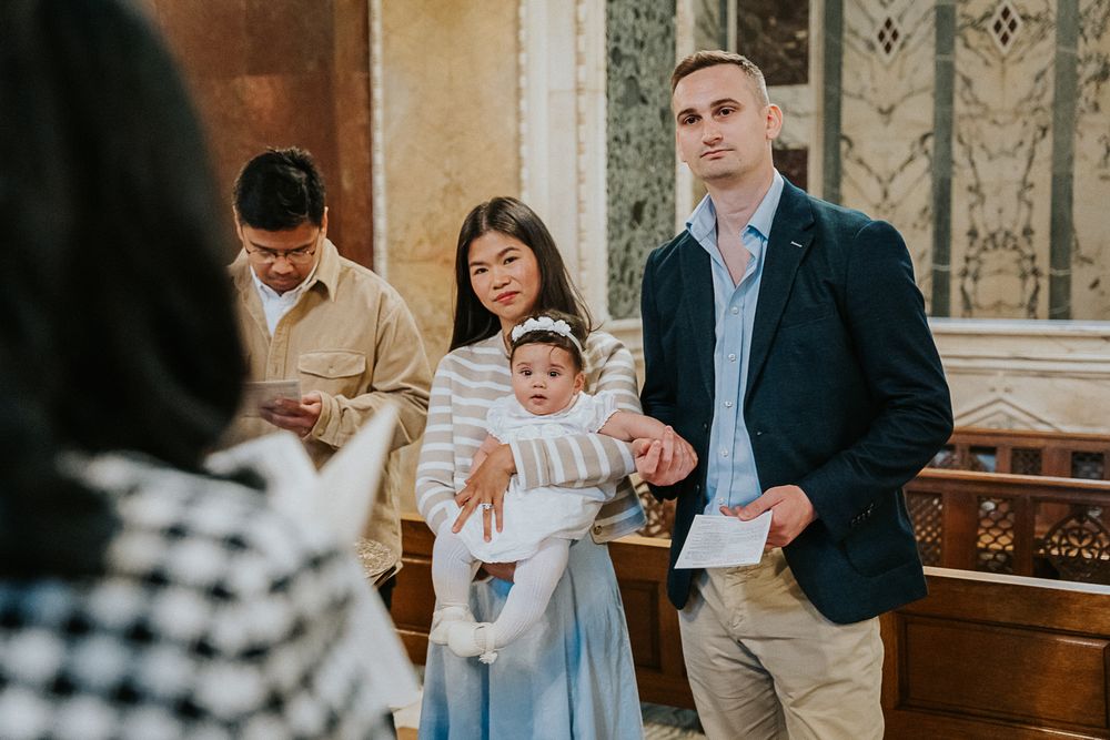 People gather at a church for a religious ceremony or baptism with ornate decorative walls in the background.